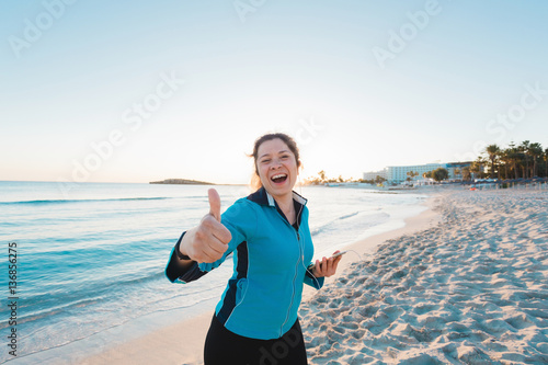 Smiling female runner show thumbs up. Summer day on the beach photo
