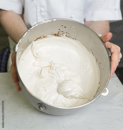 A beautiful rich and creamy , white whipped meringue mixture in a large metal mixing bowl.