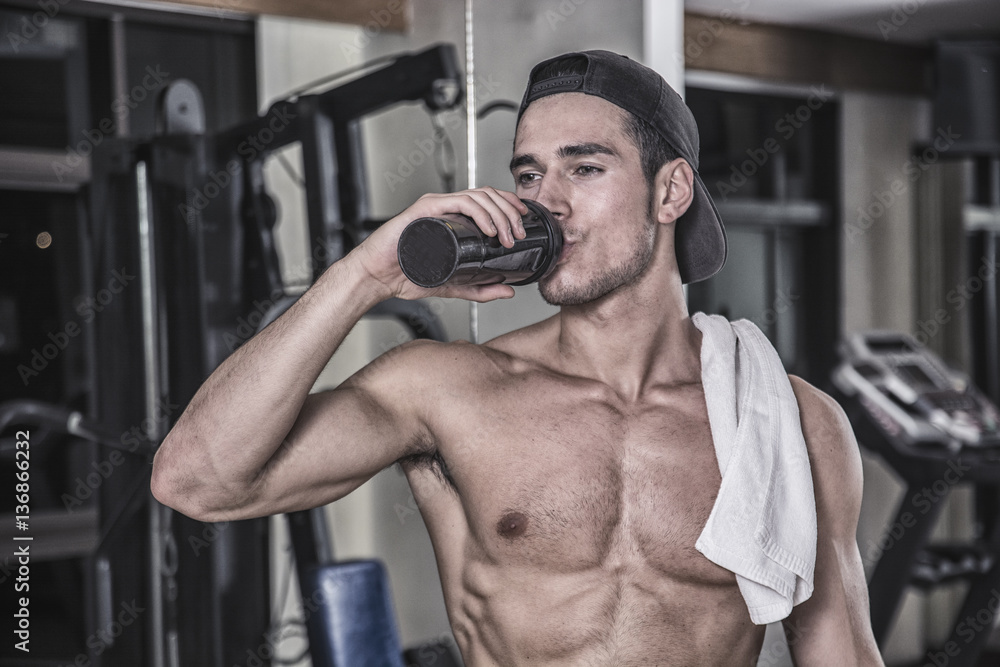 Shirtless young man drinking protein shake in gym Photograph by