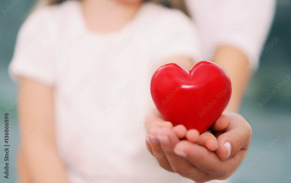 Hands of child and adult woman holding red heart, closeup