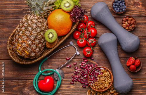Stethoscope with dumbbells and healthy food on wooden background