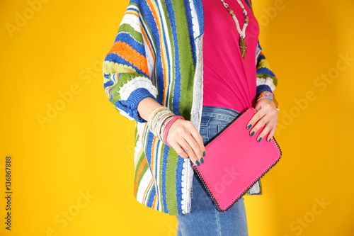 Fashion concept. Young woman holding red clutch on yellow background, closeup
