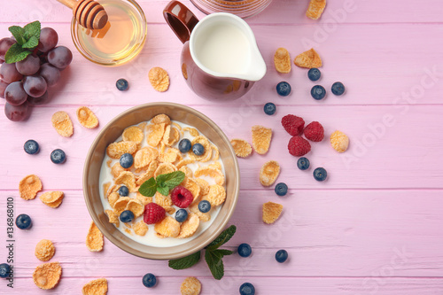 Tasty cornflakes with raspberries and blueberries on pink background