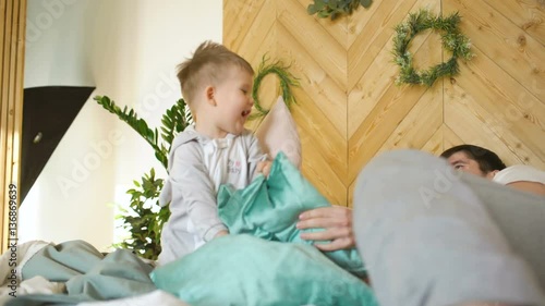 Positive father and son having fun and fight piloows on bed at home photo