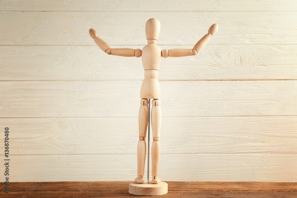 Wooden mannequin with raised hands on table, light background Wooden mannequin with raised hands on table, light background