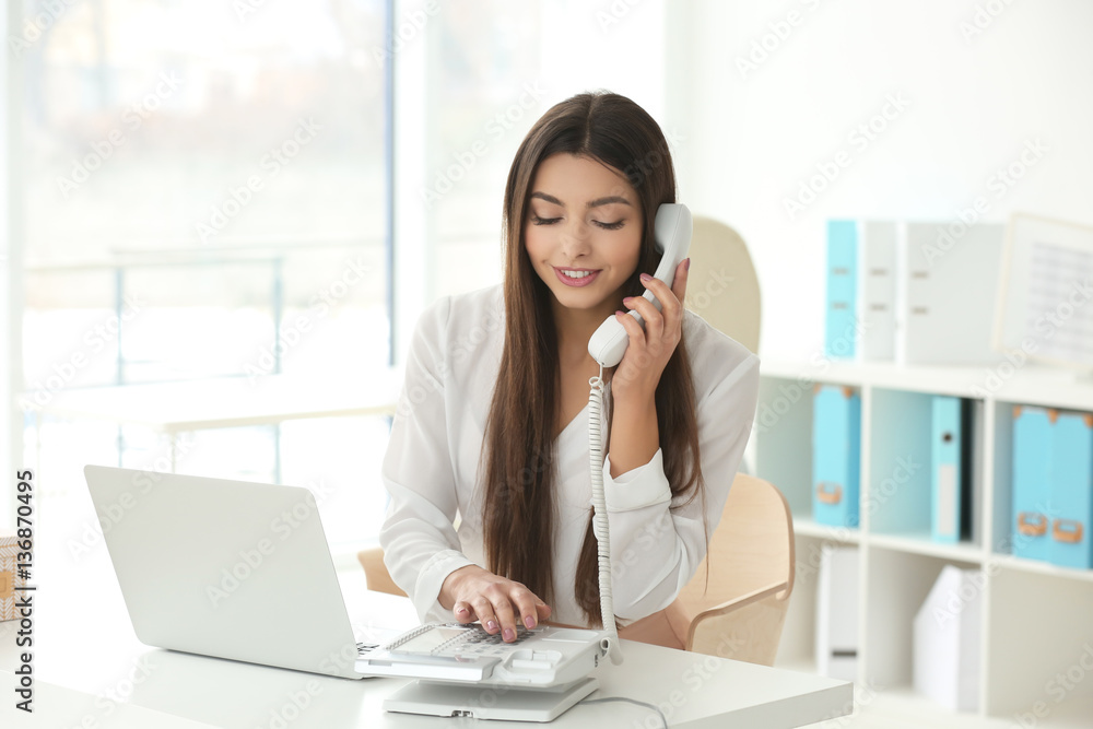 Beautiful young woman talking by telephone while working in office Beautiful young woman talking by telephone while working in office
