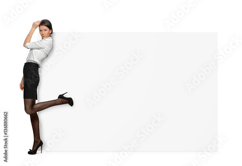 Businesswomen on white background standing with one leg raised back and leaning on a large white signboard. © gearstd