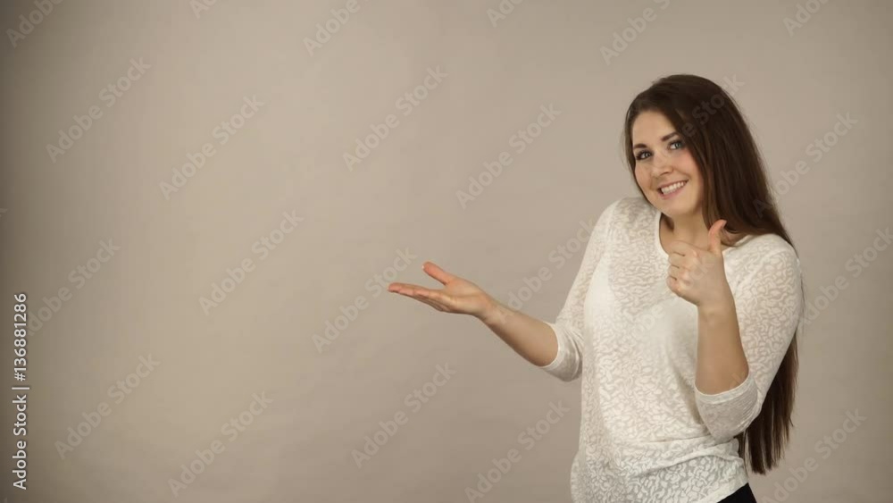 Woman showing presenting, long haired fashionable girl holding empty hand palm copy space for product, making thumb up gesture sign. Advertisement concept. Studio shot, 4K ProRes HQ codec Woman showing presenting, long haired fashionable girl holding empty hand palm copy space for product, making thumb up gesture sign. Advertisement concept. Studio shot, 4K ProRes HQ codec