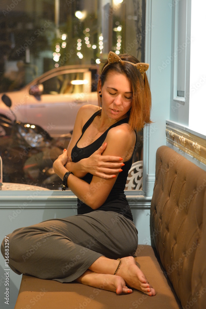 Young brunette woman in a black shirt and gray skirt sitting in a cafe. Girl hugging herself. Cat's ears Young brunette woman in a black shirt and gray skirt sitting in a cafe. Girl hugging herself. Cat's ears