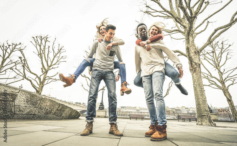 Obraz premium Happy multiracial friends couples having fun with piggiback in winter time waiting spring - Friendship concept with multicultural young people with funny attitude - Retro desaturated contrast filter