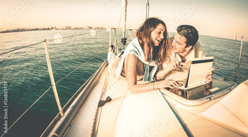 Young couple in love on sail boat having fun with tablet - Happy luxury lifestyle on yacht sailboat - Always connected people interacting with satellite wifi connection - Warm retro contrast filter © Mirko Vitali
