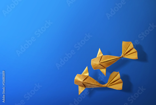 Handmade paper craft gold color origami koi carp fish on blue background with empty space. 