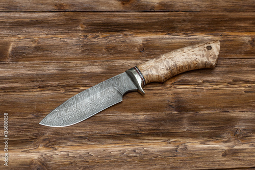 Hunting damascus steel knife handmade on a wooden background, close-up