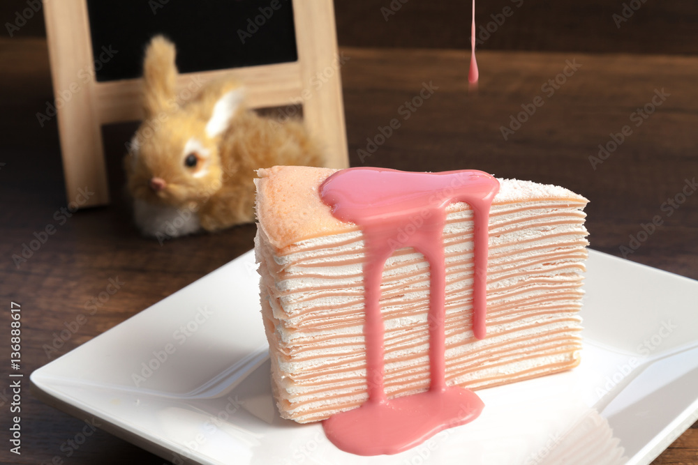 Pink crepe cake with pink custard sauce on wooden table