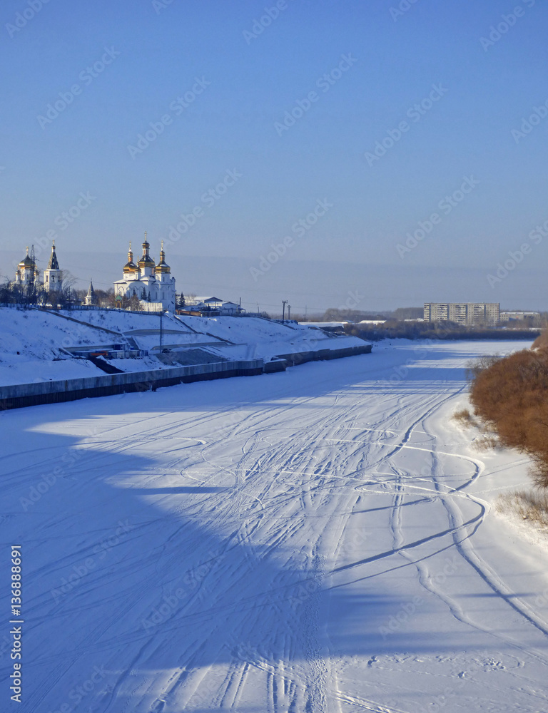 Frozen river in Siberia, Russia. Lot of ski traces in the snow. Two churches at the horizon.