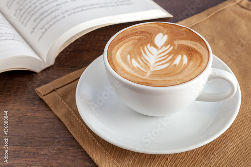 Obraz na płótnie Coffee cup of rosetta latte art on napkin with a book beside w salonie