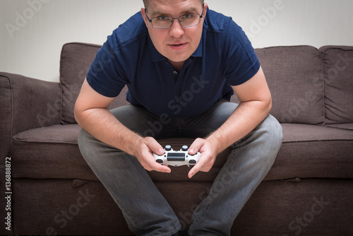 man seated on a sofa with console controller in hands and playin