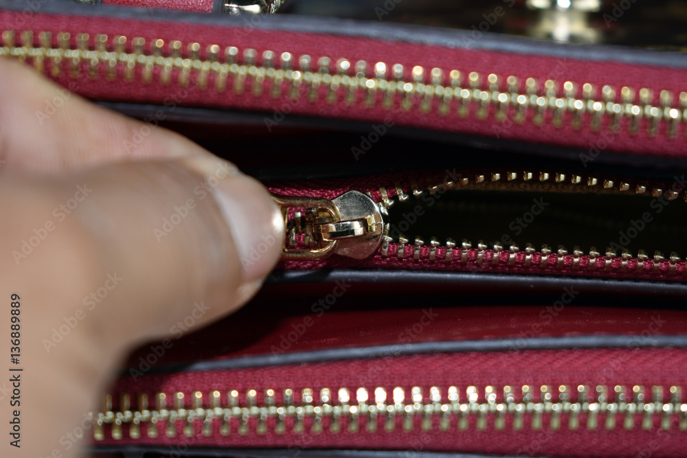 hands opening the zipper of  a secret pouch of a handbag
