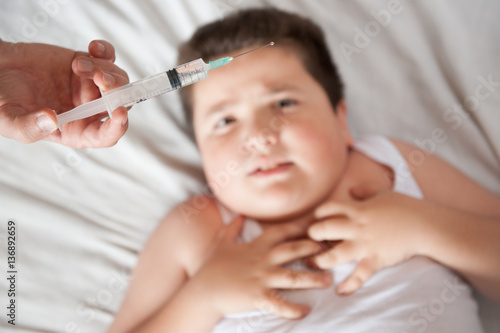 afraid fat little child lies on a background of hand with a syringe and looking at it