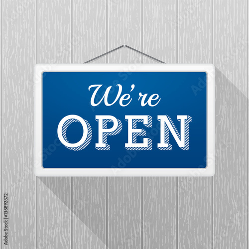 Simple blue sign with text 'we're open' hanging on a gray wooden wall. Wood texture with vertical stripes, rustic panels
