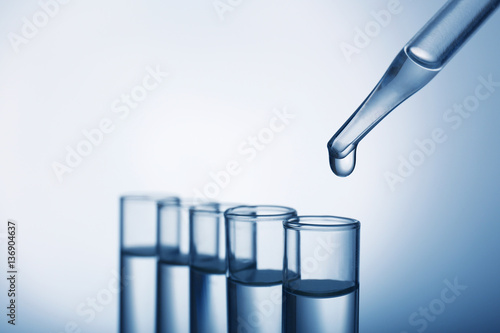 Closeup of a pipette dropping a sample into a test tube on grey background