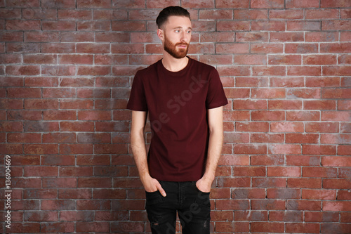Young handsome man in claret red T-shirt on brick wall background