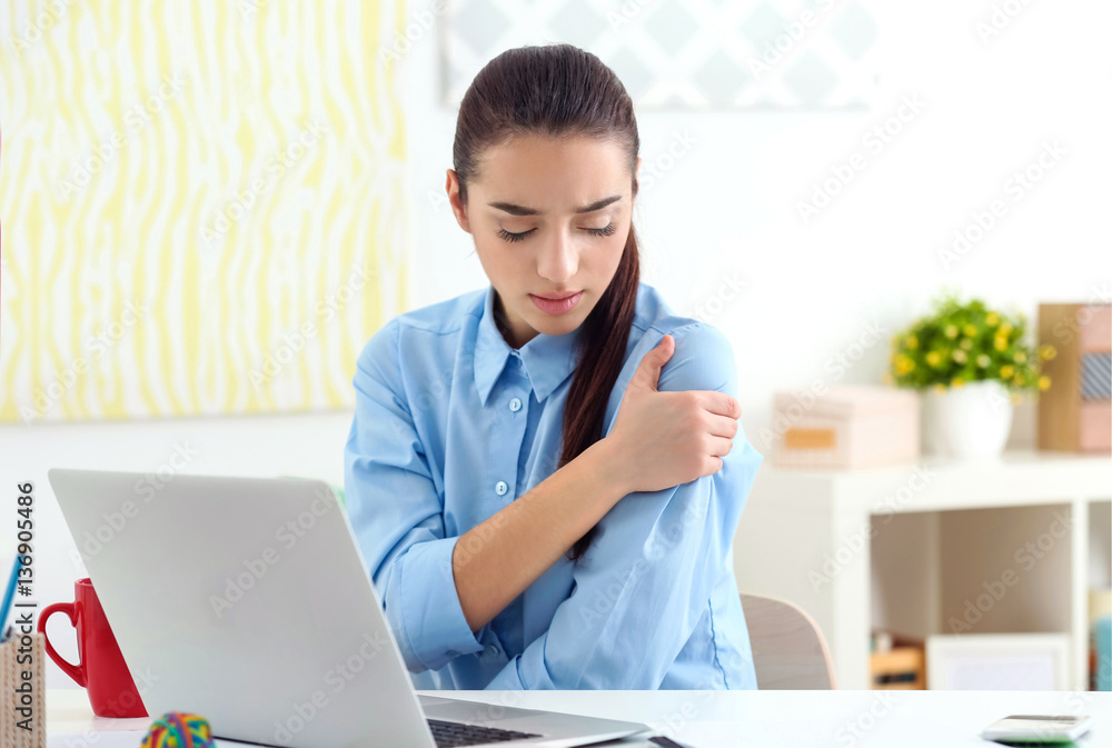 Beautiful young woman suffering from shoulder pain in office Beautiful young woman suffering from shoulder pain in office