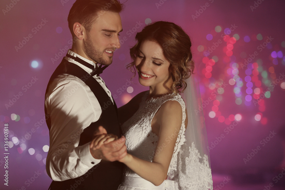 Fototapeta premium Cute happy wedding couple dancing against defocused lights