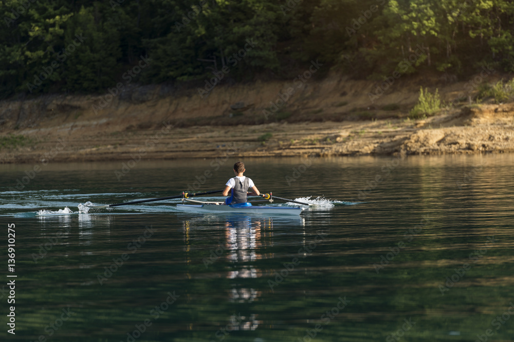 A Young single scull rowing competitor paddles on the tranquil lake A Young single scull rowing competitor paddles on the tranquil lake