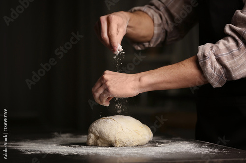 Man sprinkling flour over fresh dough on kitchen table