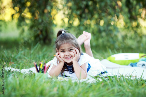 Маленькая девочка рисует лежа на траве в парке