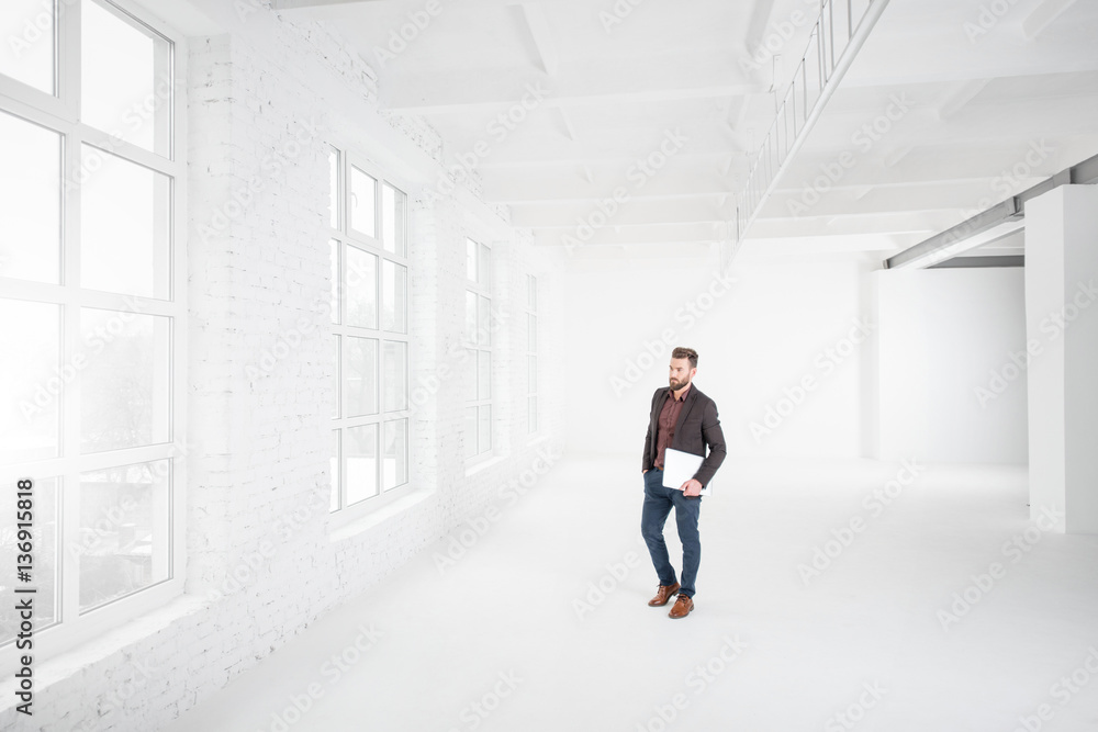 Wide shot of the white office interior with businessman walking with laptop Wide shot of the white office interior with businessman walking with laptop