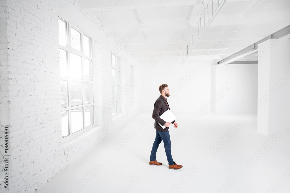 Wide shot of the white office interior with businessman walking with laptop