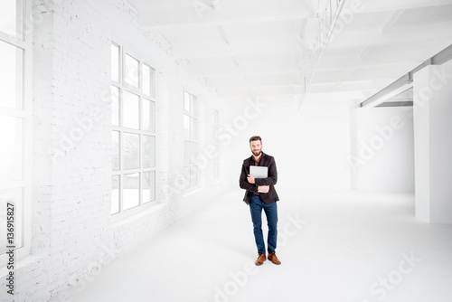 Wide shot of the white office interior with businessman standing with laptop