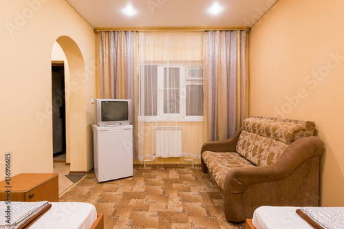 The interior of a small room with sofa bed and two single beds, window, TV and fridge