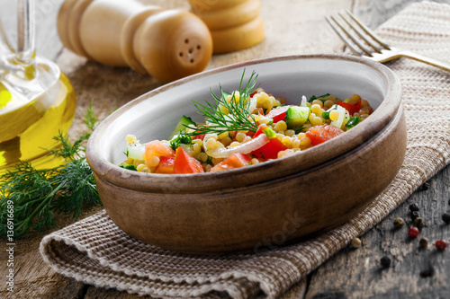 Salad made of couscous with vegetables in a bowl for healthy meal. Traditional Israeli Ptitim for lunch. Moroccan food.