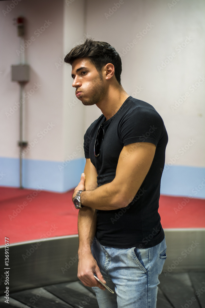 Young man standing in the airport waiting for his baggage at luggage claim belt Young man standing in the airport waiting for his baggage at luggage claim belt