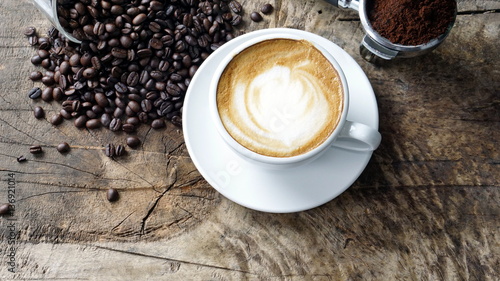 Cappuccino Coffee. A cup of latte, cappuccino or espresso coffee with milk put on a wood table with dark roasting coffee beans. Drawing the foam milk on top.