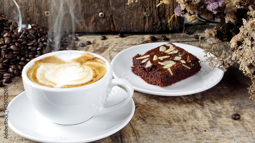 Cappuccino Coffee and sweet chocolate brownies cake. A cup of latte, cappuccino or espresso coffee with milk put on a wood table with dark roasting coffee beans. Drawing the foam milk on top.