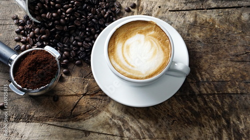 Cappuccino Coffee. A cup of latte, cappuccino or espresso coffee with milk put on a wood table with dark roasting coffee beans. Drawing the foam milk on top.
