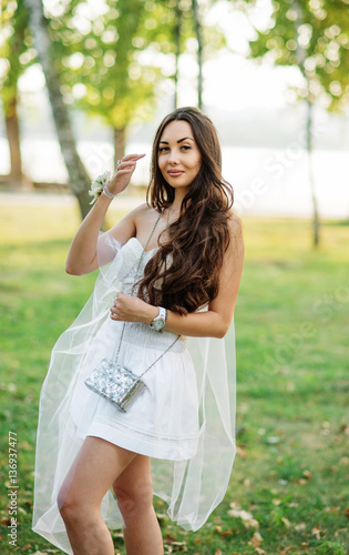 Portrait of brunette girl wearing on white dress with purse agai