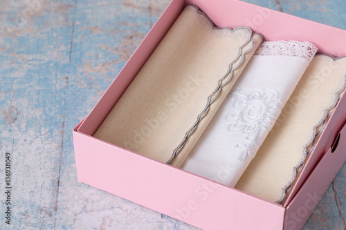  Gift for a holiday. Set handkerchiefs in a pink cardboard box on a light wooden background.