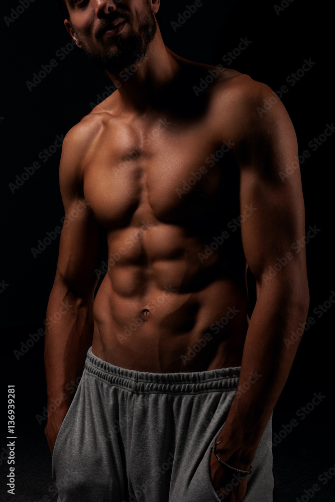 Fototapeta premium Young man showing his six pack abs with his hand in the pockets