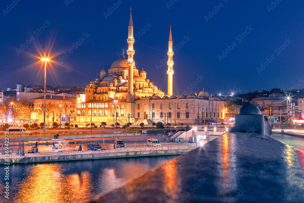 Night view at Yeni Cami Mosque worship place from Galata bridge reflected in water of Golden Horn of Bosporus. Istanbul, Turkey.