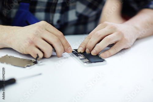 Closeup shot of male hands putting in parts to frame of opened smartphone working on white table in workshop