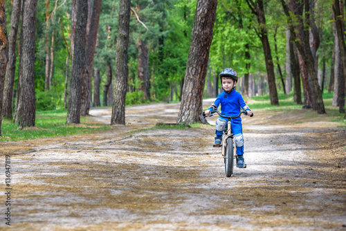 Happy cute blond kid boy having fun his first bike on sunny summer day, outdoors.  child making sports. Active leisure for children.  wear safety helmet.  is smiling and cicling. © pahis