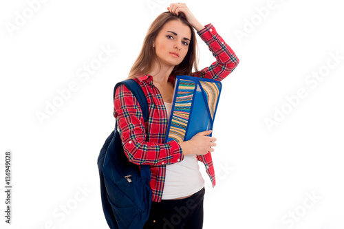 young tired brunette student woman with blue backpack on her shoulder and folder for notebooks in hands looking at the camera isolated on white background