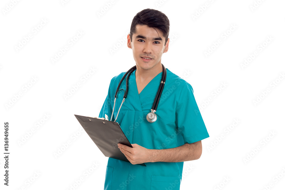 pretty young brunette male doctor with stethoscope in uniform looking at the camera and make notes isolated on white background pretty young brunette male doctor with stethoscope in uniform looking at the camera and make notes isolated on white background