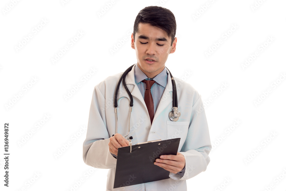 serious young brunette male doctor with stethoscope in uniform make notes isolated on white background serious young brunette male doctor with stethoscope in uniform make notes isolated on white background