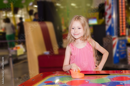 little girl standing and playing air hockey at indoor amusement park